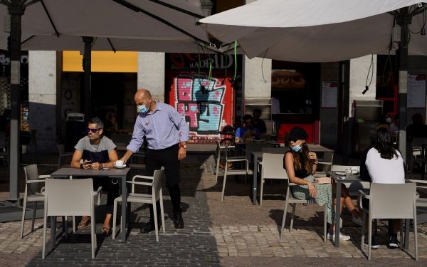 A waiter wearing a protective face mask serves a beverage for a client at an outdoor seating section of a restaurant that reopened for the first time in more than 2 months amid the coronavirus disease (COVID-19) outbreak, at Plaza Mayor Square in Madrid, Spain on May 25, 2020. (REUTERS Photo)