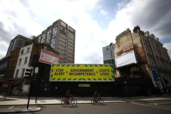 An anti-government poster is seen in London as cyclists pass, following the outbreak of the coronavirus disease (COVID-19), London, Britain on May 27, 2020. (REUTERS Photo)