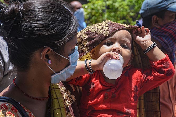 A mother looks at her child drinking water while waiting along with other migrants for city buses to reach a railway station in Surat. Photograph: PTI Photo