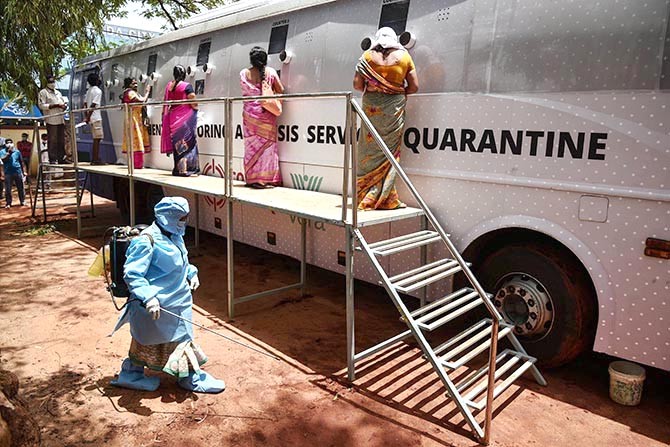 A worker sanitses an area as people wait to undergo COVID-19 tests at a mobile swab collection bus in Vijayawada. Photograph: PTI Photo