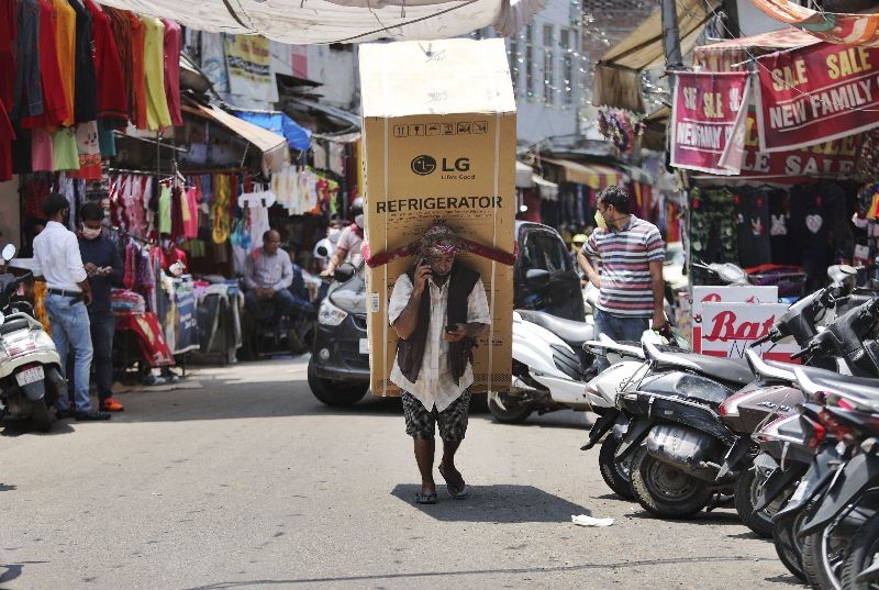 An Indian laborer talks on his mobile phone as he transports a refrigerator on his back at a market in Jammu, India, Sunday, June 7, 2020. India whose coronavirus caseload is fifth highest in the world has partially restored trains and domestic flights and allowed reopening of shops and manufacturing. (Photo by Channi Anand/AP Photo)