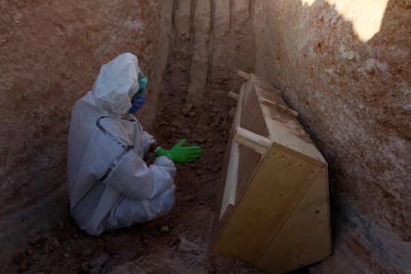 Forces (PMF), who volunteered to work in the cemetery, wearing a protective suit, reads a verse from the Koran near the coffin of a man who passed away due to the coronavirus disease (COVID-19), during his burial at the new Wadi Al-Salam cemetery, which is dedicated to those who died of the coronavirus disease (COVID-19), on the outskirts of the holy city of Najaf, Iraq on May, 25. 2020. (REUTERS File Photo)