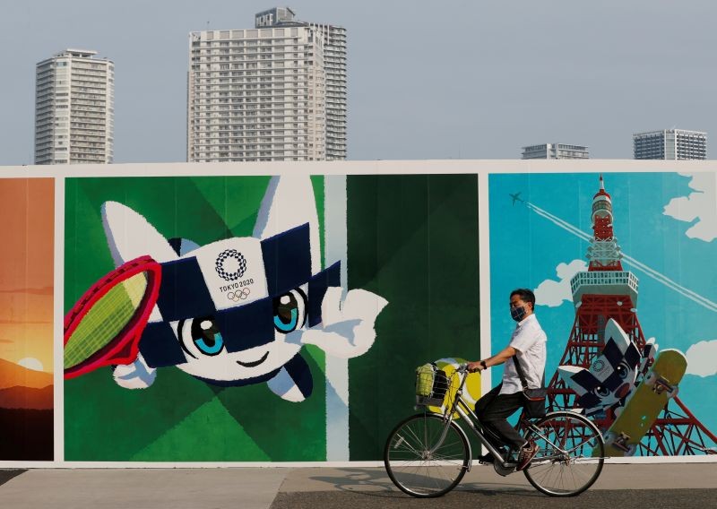 A man wearing a protective mask rides his bicycle past a large poster featuring Tokyo 2020 Olympic Games mascot Miraitowa amid the coronavirus disease (COVID-19) outbreak in Tokyo, Japan June 4, 2020. REUTERS/Kim Kyung-Hoon/Files