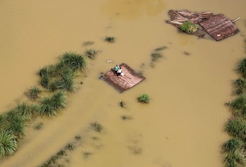 People affected by flooding stand on a partially submerged house as they wait to receive food parcels in the outskirts of Allahabad, India, August 25, 2016. REUTERS/Jitendra Prakash/File photo