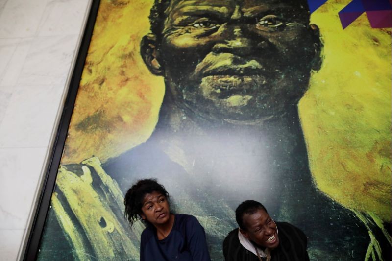 Homeless people observe the demonstrators protesting against statements that minimize racism in Brazil given by the new president of the Palmares Foundation, Sergio Nascimento de Camargo, in front of image of a Quilombola leader known as Zumbi, at the headquarters of the Palmares Foundation in Brasilia, Brazil on November 28, 2019. (REUTERS File Photo)