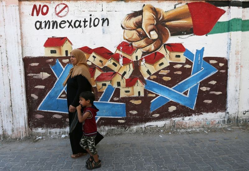 A Palestinian woman walks with her son past a mural in protest of Israel's plan to annex parts of the Israeli-occupied West Bank, in Rafah in the southern Gaza Strip on July 14, 2020. (REUTERS Photo)