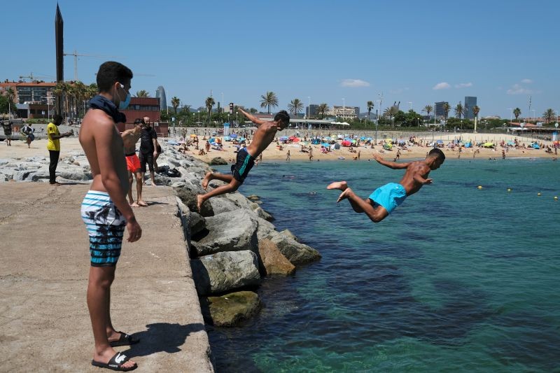 Men jump into the water as they enjoy the sunny weather at the beach, after Catalonia's regional authorities and the city council announced restrictions to contain the spread of the coronavirus disease (COVID-19) in Barcelona, Spain on July 19, 2020. (REUTERS Photo)