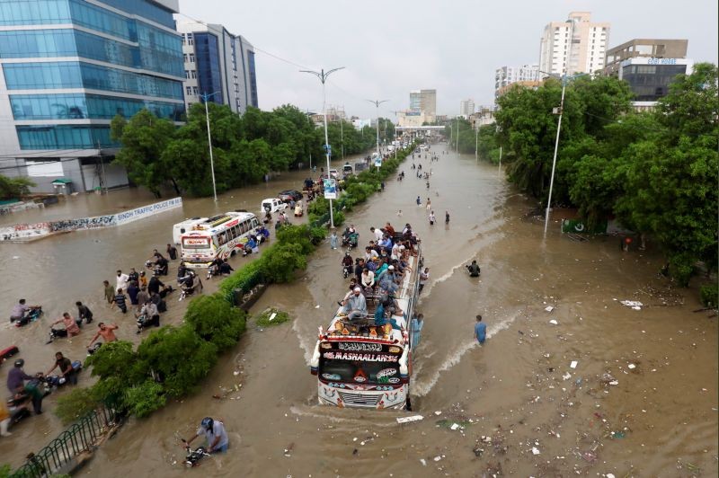 People sit atop a bus roof while others wade through the flooded road during monsoon rain, as the outbreak of the coronavirus disease (COVID-19) continues, in Karachi, Pakistan on August 27, 2020. (REUTERS Photo)