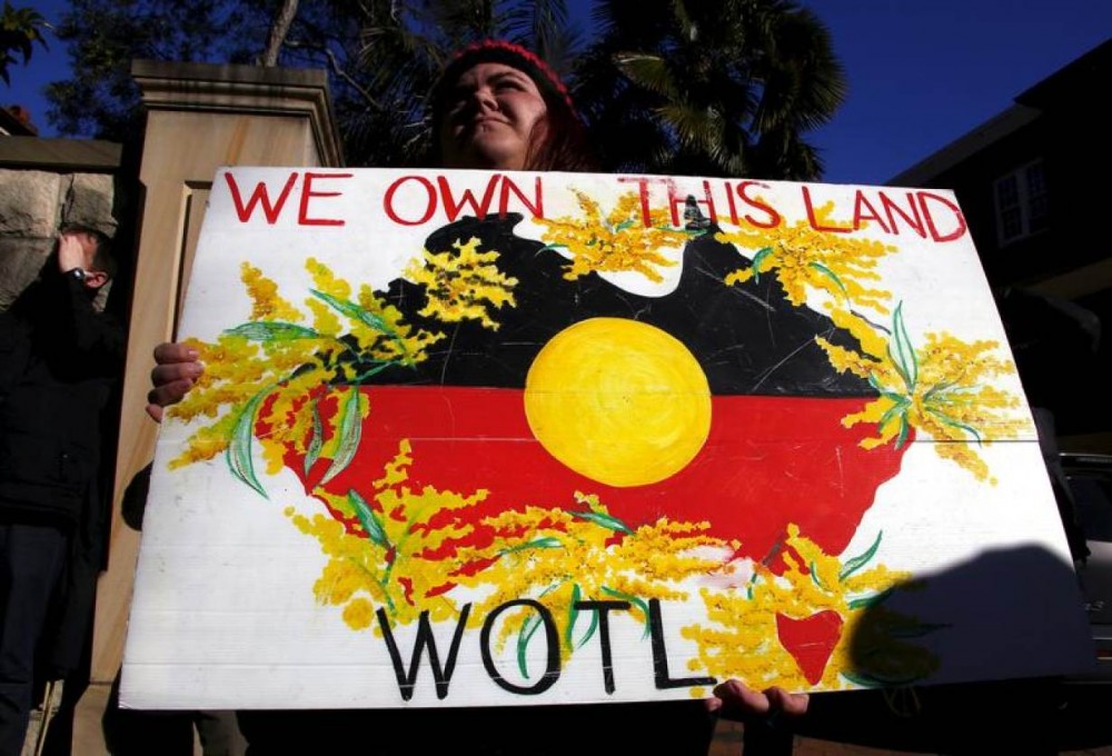 FILE PHOTO: A protester holds a placard as she stands outside the venue for a meeting between Australia's Prime Minister Tony Abbott and forty of the nation's most influential Indigenous representatives in Sydney, Australia, July 6, 2015. REUTERS/David Gray
