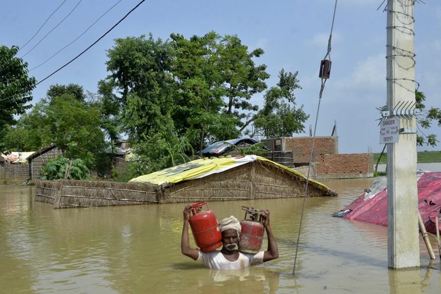 A man carries gas cylinders as he wades through a flooded area following heavy monsoon rains in Muzaffarpur in Bihar. (Image: AFP)