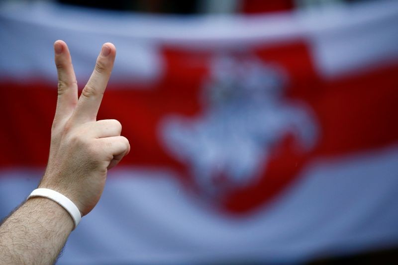 A person flashes the victory sign in front of a historical white-red-white flag of Belarus while attending an opposition demonstration to protest against presidential election results at the Independence Square in Minsk, Belarus on August 25, 2020. (REUTERS Photo)