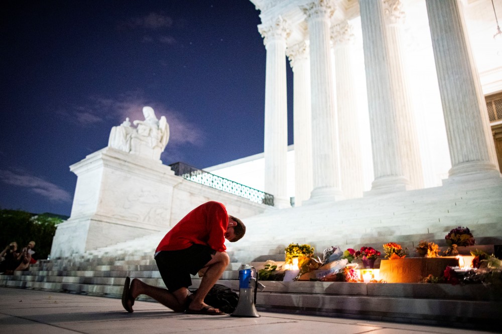 A man kneels as he brings a megaphone to a vigil on the steps of the U.S. Supreme Court following the death of U.S. Supreme Court Justice Ruth Bader Ginsburg, in Washington, U.S., September 18, 2020. REUTERS/Al Drago