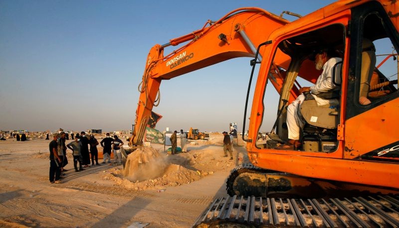 A construction vehicle digs up the corpse of a man who, according to his relatives, died of the coronavirus disease (COVID-19), to be transferred to the "Valley of Peace" cemetery on the outskirts of the holy city of Najaf, Iraq September 12, 2020.  (REUTERS Photo)
