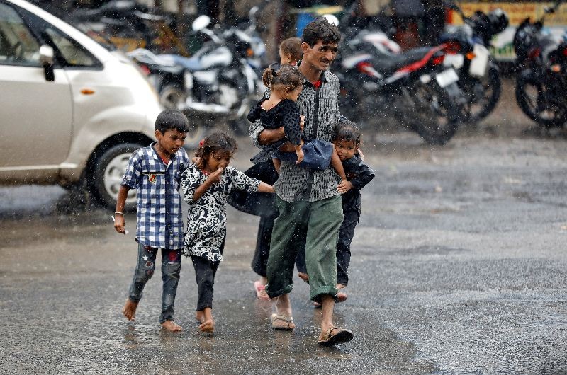 A man carrying children crosses a road during heavy rains in Ahmedabad, India, August 31, 2020. REUTERS/Amit Dave