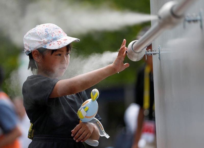 FILE PHOTO: A visitor experiences a large-scale misting tower dispensing ultra-fine mist during a proving test of heat countermeasures for the Tokyo 2020 Olympic and Paralympic Games at the venue of FIVB Beach Volleyball World Tour, also acting as a test event for the games, in Tokyo, Japan July 25, 2019. REUTERS/Issei Kato/File Photo