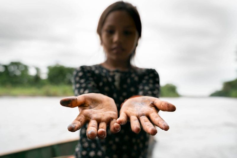 An indigenous girl's hands are stained from crude oil after playing along the riverbanks near the community of San Pedro de Río Coca, Sucumbios, northern Ecuadorian Amazon, April 18 2020. Telmo Ibarburu/Amazon Frontlines