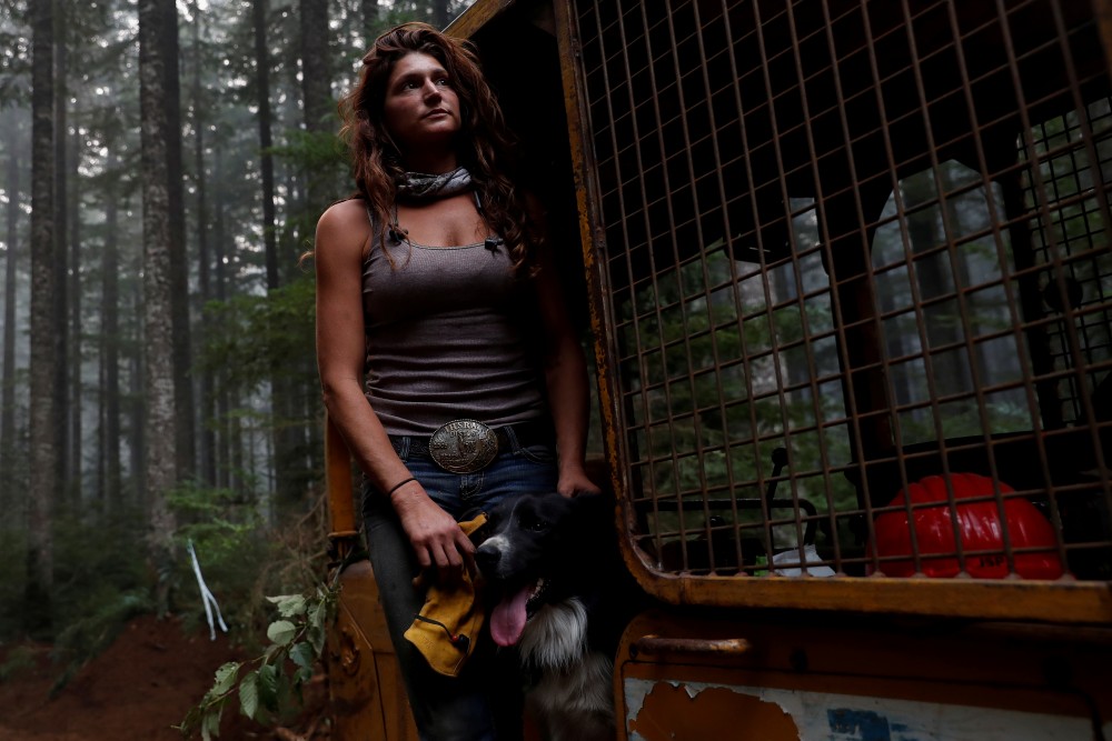 Nicole West, part of the Hillbilly Brigade of some 1,200 men and women who spontaneously came together to fight fires, stands for a portrait petting her dog Oink on a bulldozer during the aftermath of the Riverside Fire near Molalla, Oregon, U.S., September 16, 2020. Picture taken on September 16. (REUTERS/Shannon Stapleton)