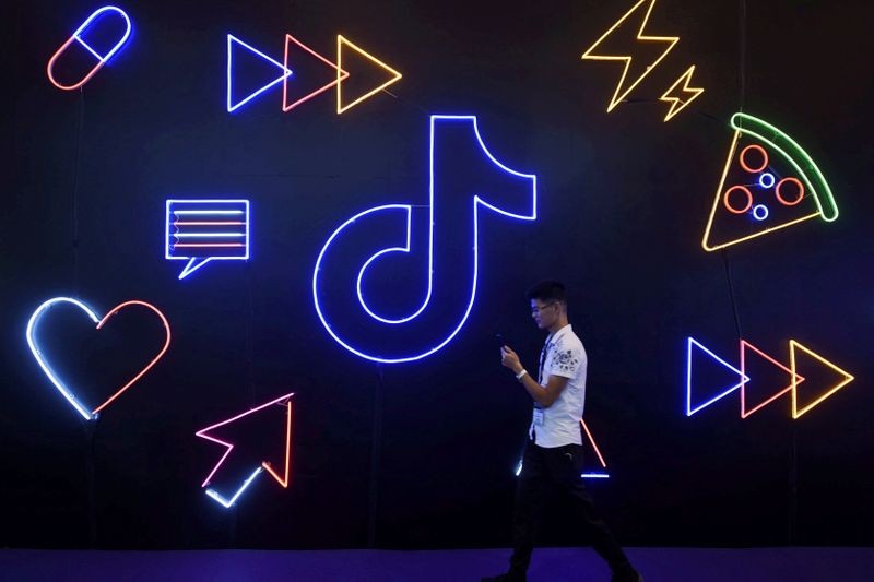 FILE PHOTO: A man holding a phone walks past a sign of Chinese company ByteDance's app TikTok, known locally as Douyin, at the International Artificial Products Expo in Hangzhou, Zhejiang province, China October 18, 2019. REUTERS/Stringer