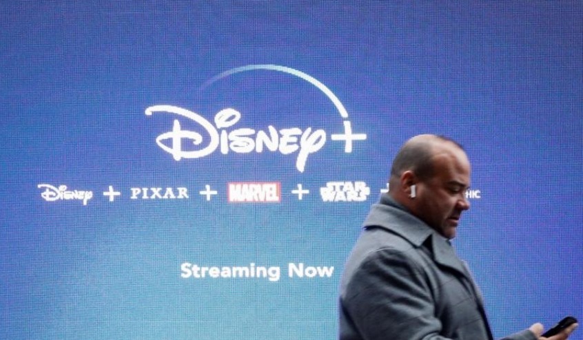 FILE PHOTO: A man looks at his phone as he passes by a screen advertising Walt Disney's streaming service Disney+ in New York City, U.S., November 12, 2019. REUTERS/Brendan McDermid