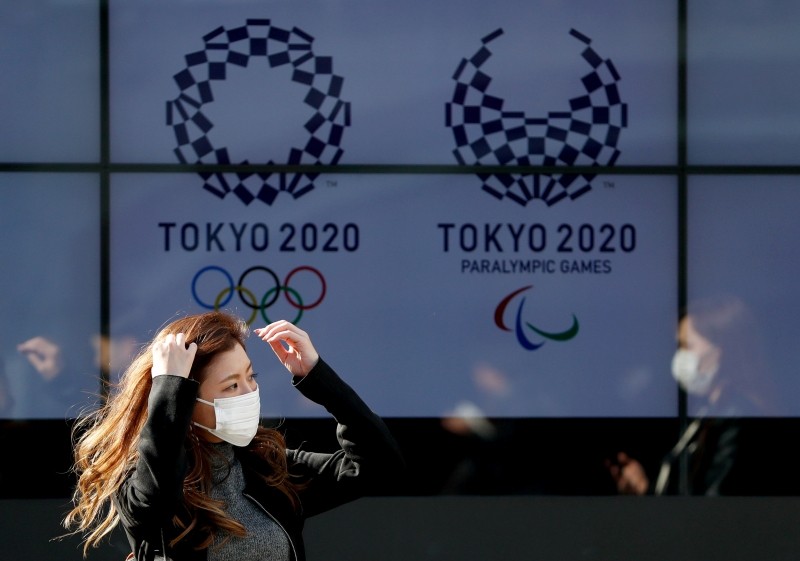 FILE PHOTO: A passerby wearing a protective face mask following an outbreak of the coronavirus disease (COVID-19) walks past a screen displaying logos of Tokyo 2020 Olympic and Paralympic Games in Tokyo, Japan March 19, 2020. REUTERS/Issei Kato/File Photo