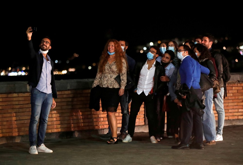 FILE PHOTO: People pose for a selfie in Naples, where masks are required outdoors 24 hours a day and bars and restaurants are required to close at 11.00.p.m. (2100GMT), as part of efforts to contain the coronavirus disease (COVID-19) outbreak, Italy October 6, 2020. REUTERS/Ciro De Luca/File Photo