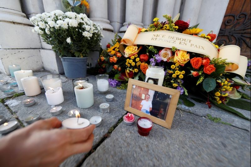A woman puts a candle near a picture of Vincent Loques, sexton of the Notre Dame church, one of the victims of a deadly knife attack, in front of the Notre Dame church in Nice, France, October 30, 2020. (REUTERS Photo)