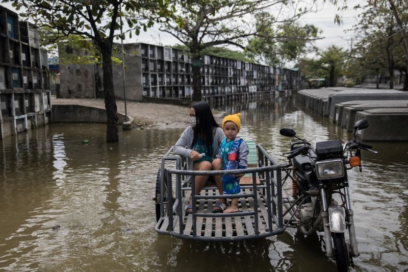 A woman and a boy stay on a rickshaw while a relative lights a candle for their departed loved one in a flooded cemetery following Typhoon Molave, in Masantol, Pampanga, Philippines. (Reuters Photo)