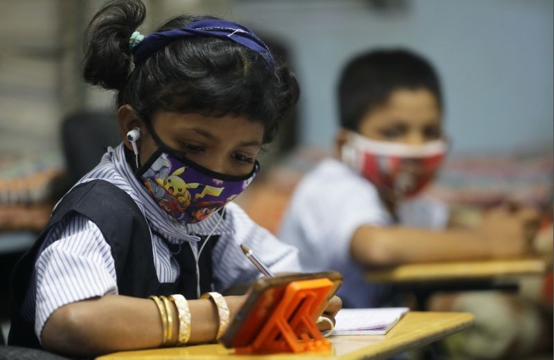 A student wearing a protective mask writes notes from an online lecture on a mobile phone, inside a digital mobile education library, initiated to provide mobile phones to chidren who have no access to them for their education classes amidst the spread of the coronavirus disease (COVID-19) in Mumbai on October 16, 2020. (REUTERS Photo)