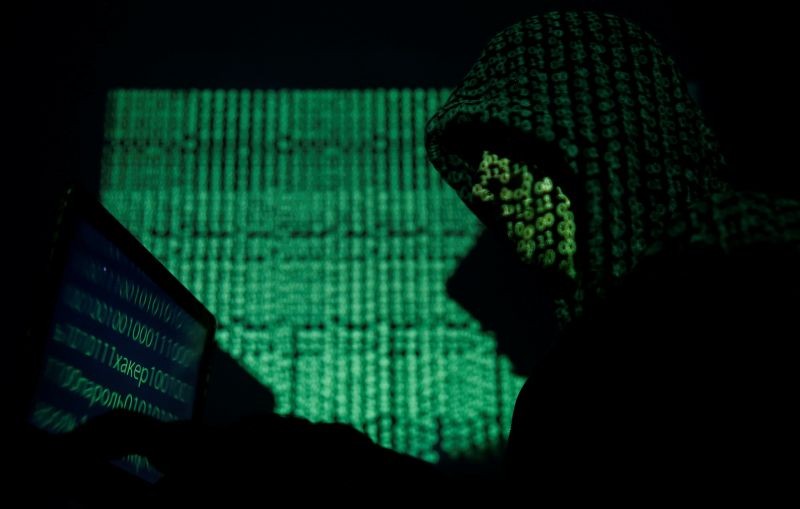 A hooded man holds a laptop computer as cyber code is projected on him in this illustration picture taken on May 13, 2017. (REUTERS File Photo)