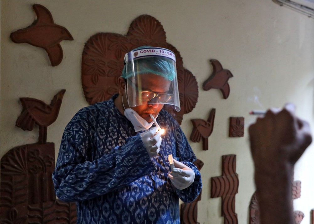 FILE PHOTO: A man wearing a protective face shield smokes outside the Indian Coffee House after it was re-opened, after authorities eased lockdown restrictions that were imposed to slow the spread of the coronavirus disease (COVID-19), in Kolkata, India, July 2, 2020. REUTERS/Rupak De Chowdhuri