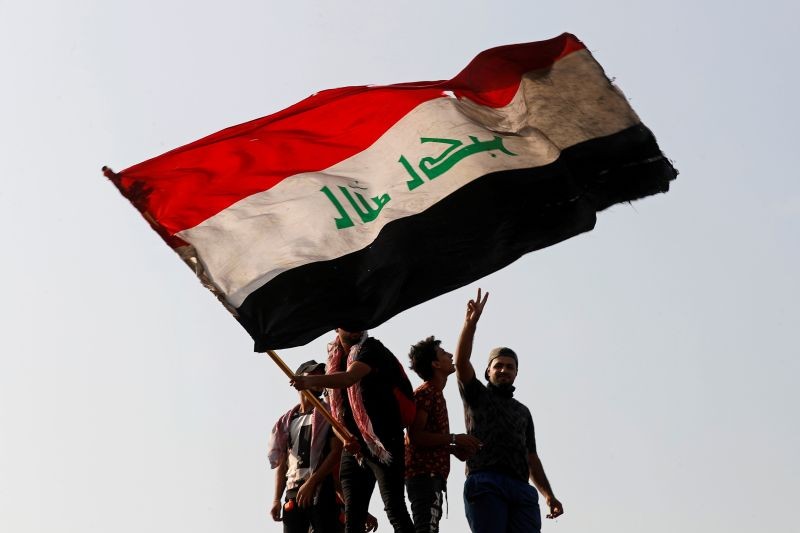 A demonstrator holds an Iraqi flag as another gestures while they gather to mark the first anniversary of the anti-government protests in Baghdad, Iraq October 25, 2020. (REUTERS Photo)