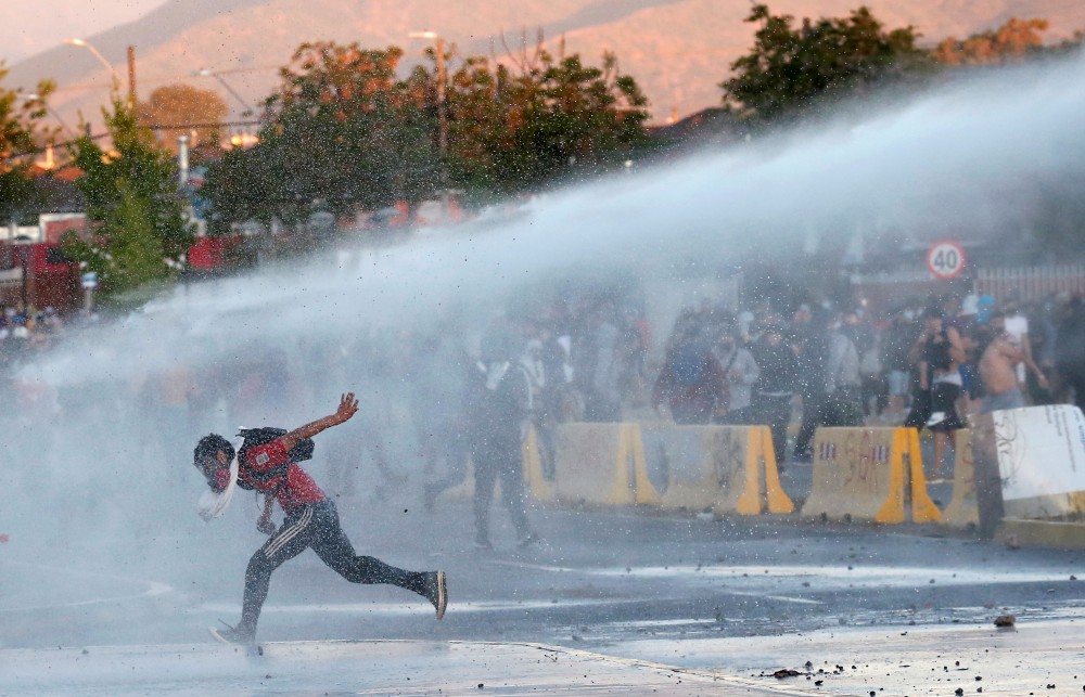A demonstrator is sprayed by riot police water cannon during a protest against Chile's government, on the one-year-anniversary of the protests and riots in 2019, in Quilpue, Chile October 18, 2020. REUTERS/Rodrigo Garrido