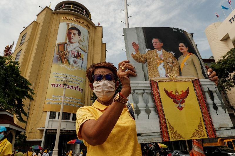 A royalist holds a picture of Thailand's late King Bhumibol Adulyadej and Queen Mother Sirikit in front of an image of King Maha Vajiralongkorn hanging on the facade of the Deves Insurance Building in Bangkok, Thailand, October 14, 2020. REUTERS/Jorge Silva