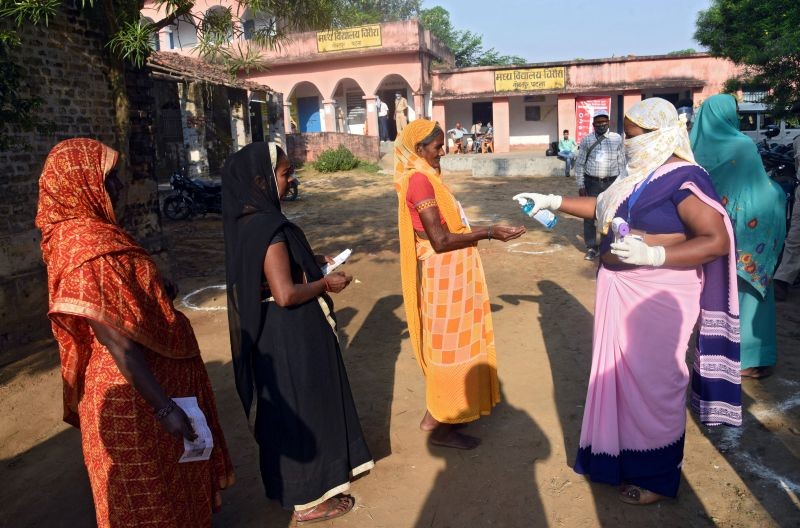 A woman sprays sanitizer on a voter's hand as she and others wait in a queue to cast their vote outside a polling booth during the state assembly election, amidst the spread of the coronavirus disease (COVID-19), at a village on the outskirts of Patna, in the eastern state of Bihar, India, October 28, 2020. (REUTERS Photo)