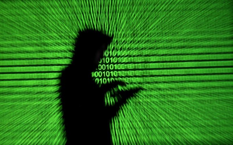 Silhouette of mobile device user is seen next to a screen projection of binary code are seen in this picture illustration taken on March 28, 2018.  (REUTERS File Photo)