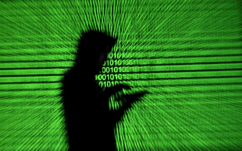 Silhouette of mobile device user is seen next to a screen projection of binary code are seen in this picture illustration taken on March 28, 2018.  (REUTERS File Photo)