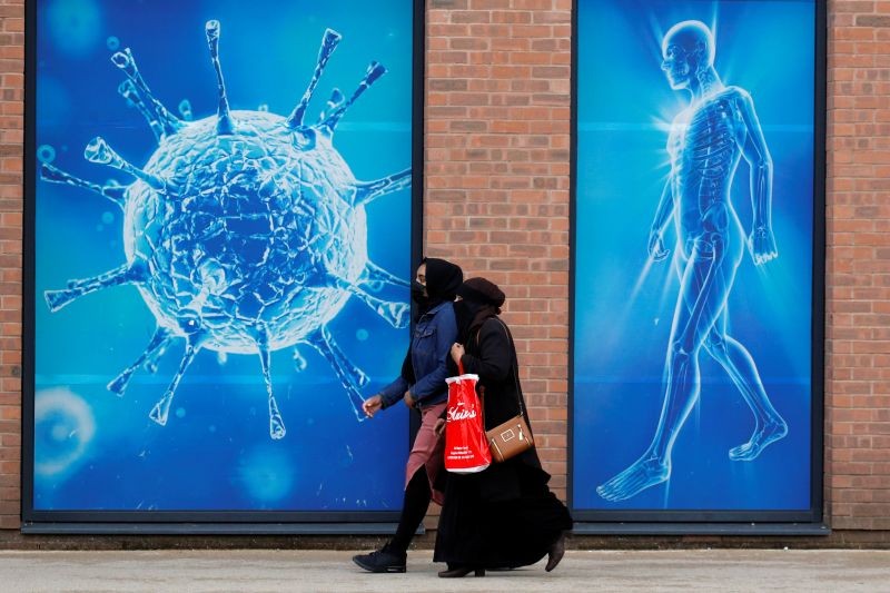 People walk past an illustration of a virus outside a regional science centre, as the city and surrounding areas face local restrictions in an effort to avoid a local lockdown being forced upon the region, amid the coronavirus disease (COVID-19) outbreak, in Oldham, Britain on August 3, 2020. (REUTERS File Photo)