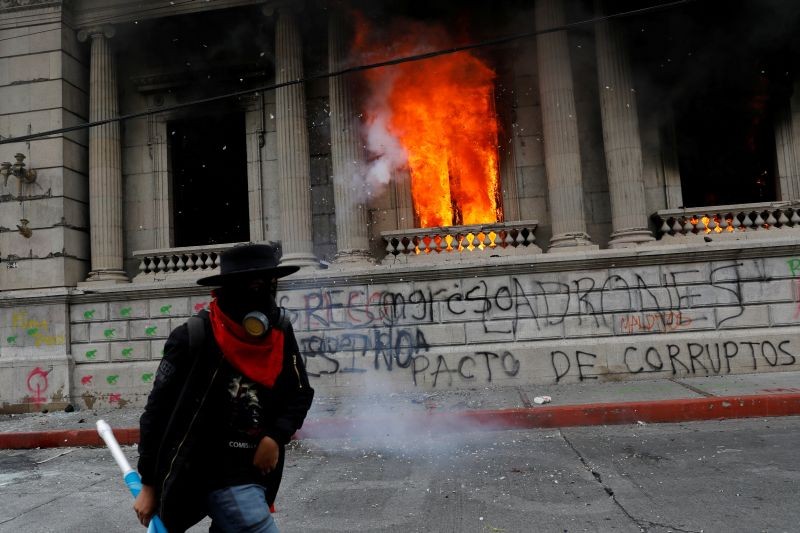 A man walks past an office of the Congress building set on fire by demonstrators during a protest demanding the resignation of President Alejandro Giammattei, in Guatemala City, Guatemala November 21, 2020. REUTERS/Luis Echeverria