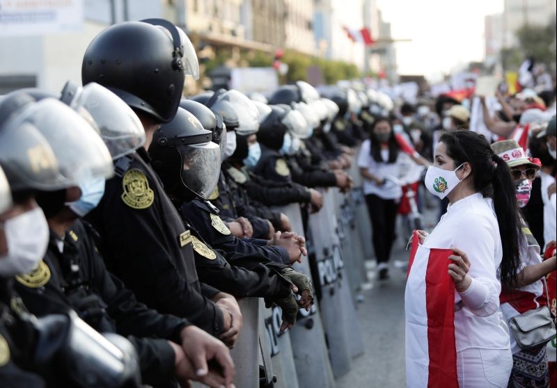 A woman holds a national flag while standing in front of police outside Congress after Peru's interim President Manuel Merino announced his resignation, in Lima, Peru November 15, 2020. (REUTERS Photo)