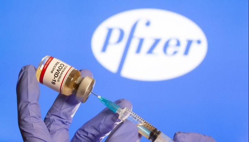 A woman holds a small bottle labeled with a "Coronavirus COVID-19 Vaccine" sticker and a medical syringe in front of displayed Pfizer logo in this illustration taken, October 30, 2020. (REUTER File Photo)