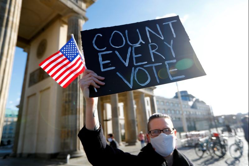A demonstrator holds a placard and a U.S. flag during the "Count the Votes! Rally for Fair Elections in the USA" organized by Young Democrats Abroad following the 2020 U.S. presidential election, next to the Brandenburg Gate, in Berlin, Germany November 4, 2020. (REUTERS Photo)