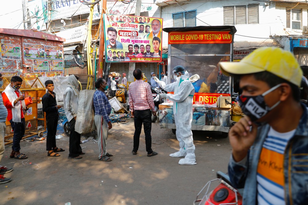 A healthcare worker wearing personal protective equipment (PPE) collects a swab sample from a man, as others stand in a queue amidst the spread of the coronavirus disease (COVID-19), at a wholesale market, in the old quarters of Delhi, November 17, 2020. REUTERS/Adnan Abidi