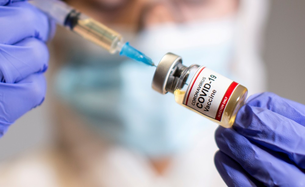 FILE PHOTO: A woman holds a small bottle labeled with a "Coronavirus COVID-19 Vaccine" sticker and a medical syringe in this illustration taken, October 30, 2020. REUTERS/Dado Ruvic