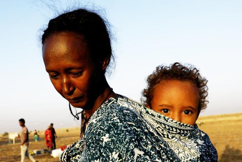 An Ethiopian woman who fled the ongoing fighting in Tigray region, carries her child near the Setit river on the Sudan-Ethiopia border in Hamdayet village in eastern Kassala state, Sudan on November 22. (REUTERS Photo)