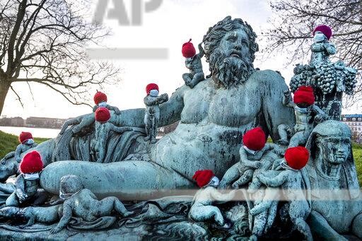 The 16 bronze children surrounding the statue Nilen, (the Nile) are decorated with face masks in Copenhagen, Wednesday, Dec. 16, 2020. Each year the children are decorated with red elves hats during the Christmas period, this year they also included face masks as a nod to the coronavirus pandemic. (Liselotte Sabroe/Ritzau Scanpix via AP)