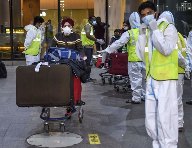 Municipal workers in personal protective equipment look on as passengers from United Kingdom arrive at the Chhatrapati Shivaji Maharaj International Airport in Mumbai. Photograph: Kunal Patil/PTI Photo