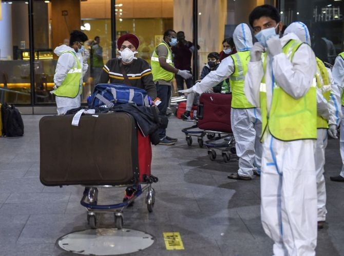 Municipal workers in personal protective equipment look on as passengers from United Kingdom arrive at the Chhatrapati Shivaji Maharaj International Airport, in Mumbai. Photograph: Kunal Patil/PTI Photo