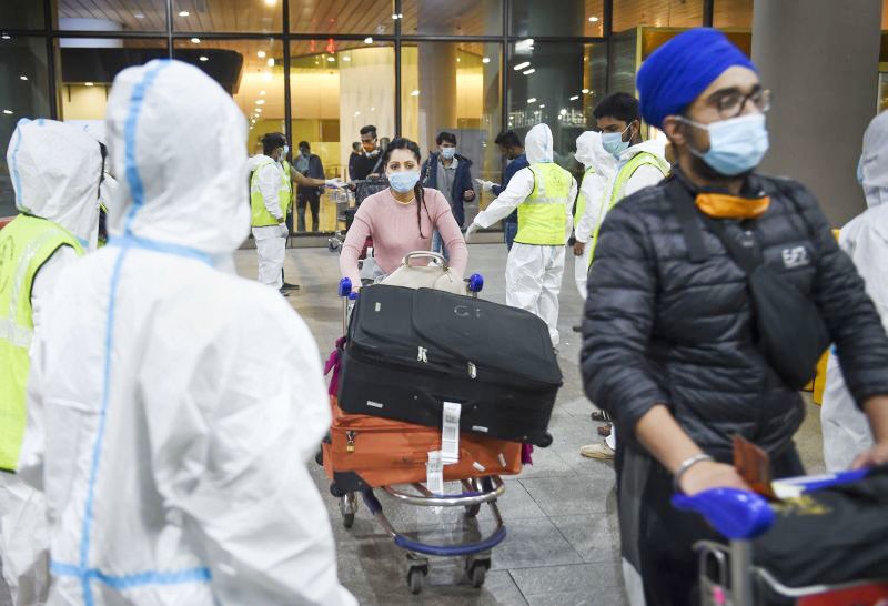 Municipal workers in personal protective equipment look on as passengers from United Kingdom arrive at the Chhatrapati Shivaji Maharaj International Airport, in Mumbai on December 22, 2020. New restrictions were put in place by authorities from 12:00 am for UK flights in the light of the new Covid-19 strain found in the country, which is said to be a super spreader and is claimed to be 70% more transmissible. Indian government has temporarily suspended all passengers' flights from the United Kingdom. (PTI Photo)