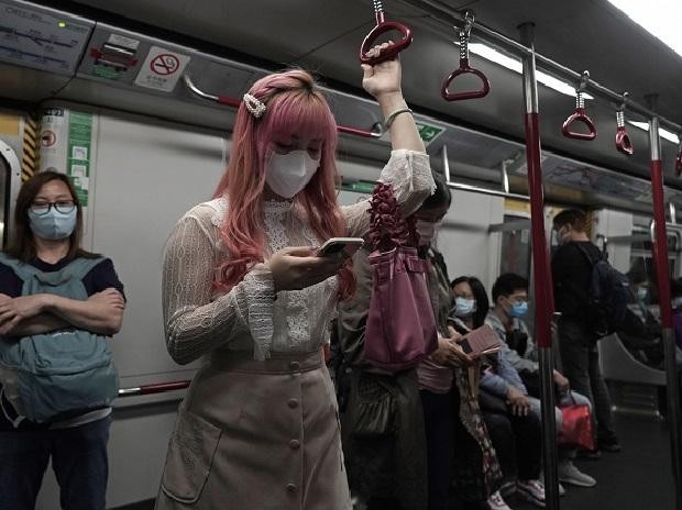 A woman wearing a face mask as a precaution against the COVID-19 while using smartphone in a subway train in Hong Kong | PTI