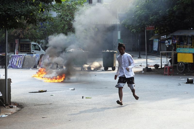 A man crosses the street while fire is seen in front of a road barricade that prevents security forces from advancing in Mandalay, Myanmar on March 14, 2021. At least four people were shot dead during protests in Myanmar on Sunday, as security forces continued their violent crackdown against dissent following last month's military coup. (AP/PTI Photo)